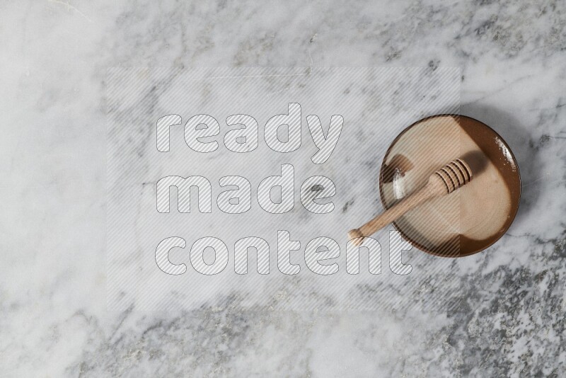 Multicolored pottery plate with wooden honey dipper in it on grey marble background
