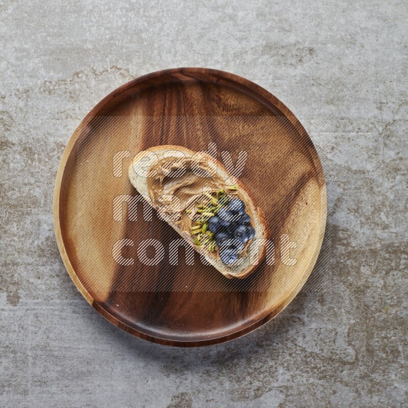 open faced peanut butter sandwich with blueberries and pistachio on a grey textured background