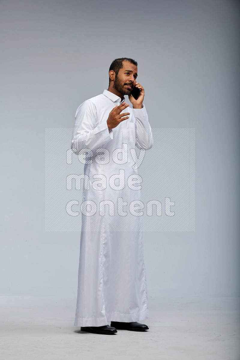 Saudi man wearing Thob standing talking on phone on Gray background
