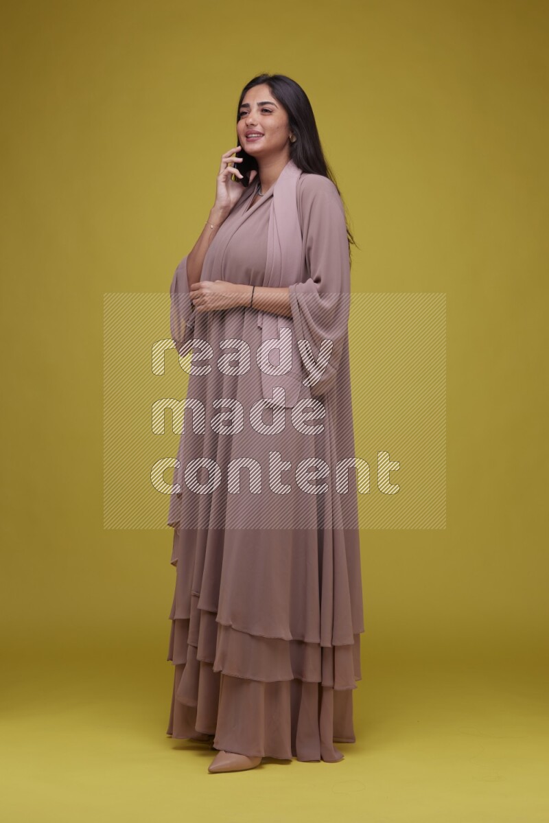 A woman Calling on a Yellow Background wearing Brown Abaya