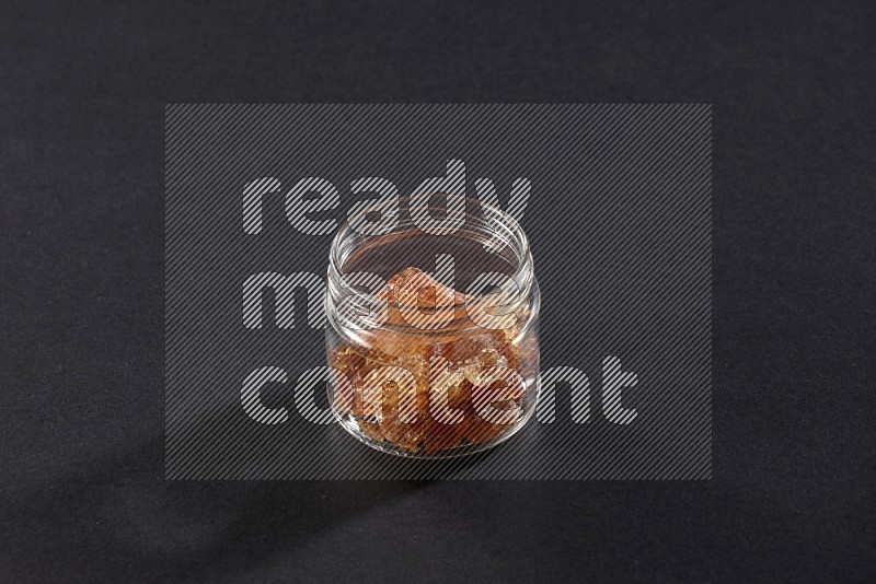 A glass jar filled with gum arabic on black flooring in different angles