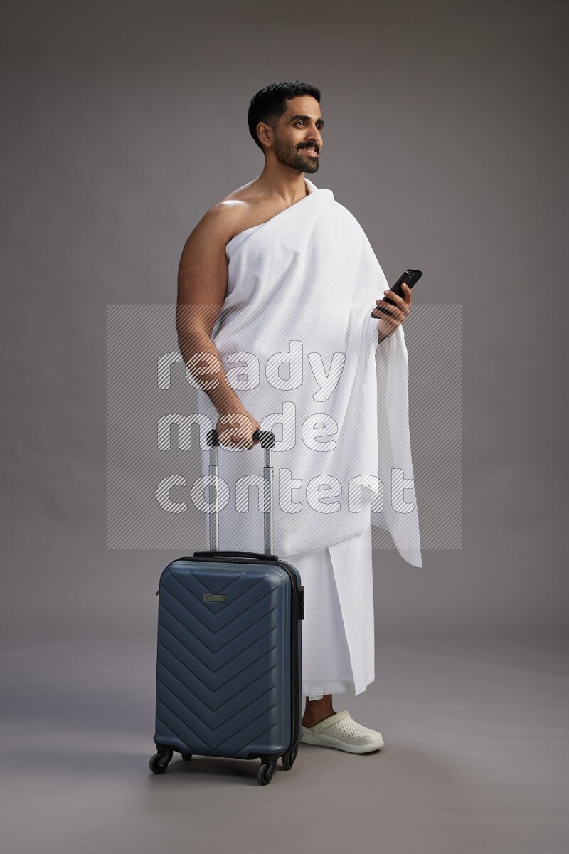 A man wearing Ehram Standing holding traveling bag on gray background