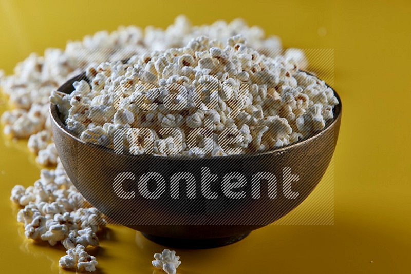 A cooper ceramic bowl full of popcorn with popcorn beside it on a yellow background in different angles