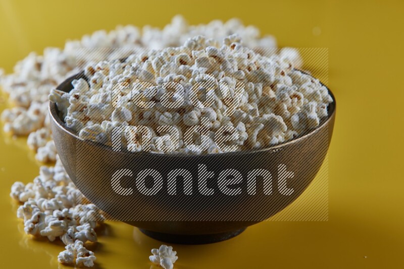 A copper ceramic bowl full of popcorn with popcorn beside it on a yellow background in different angles