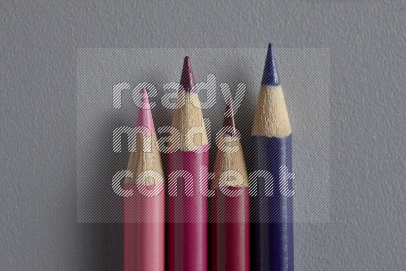 A collection of sharpened colored pencils arranged showcasing a gradient of pink and purple hues on grey background