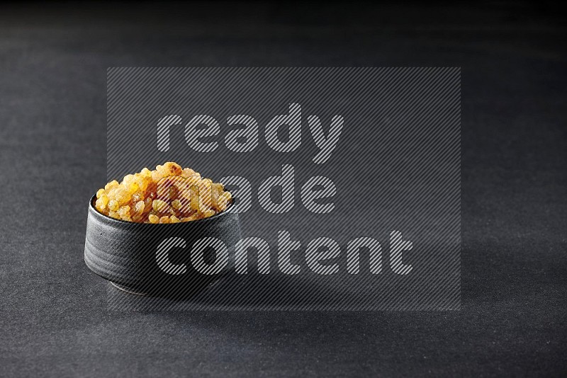 A black pottery bowl full of raisins on a black background in different angles