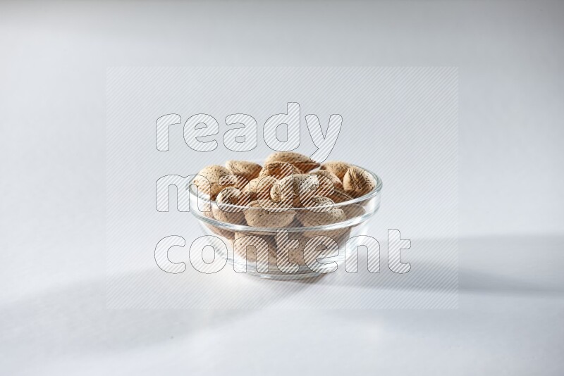 A glass bowl full of almonds on a white background in different angles