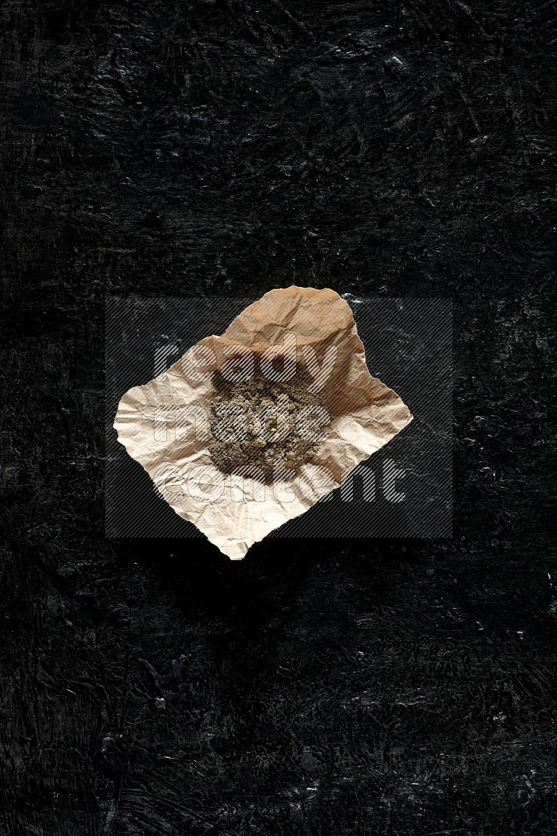 Cardamom powder in a crumpled piece of paper on textured black flooring