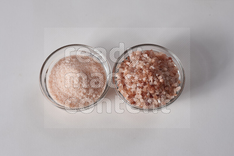 2 glass bowls one is filled with fine himalayan salt and the other with coarse himalayan salt on white background