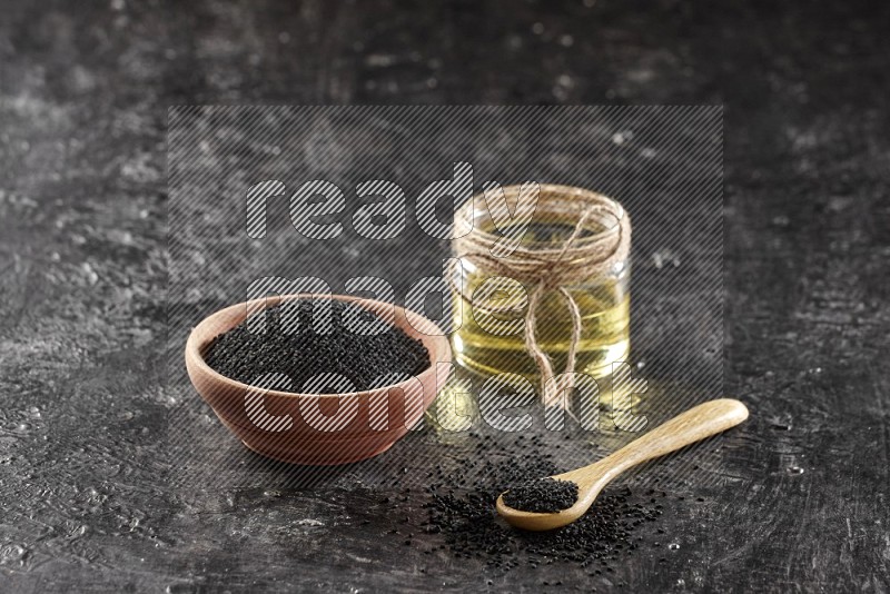 A wooden bowl and spoon full of black seeds and a glass jar of black seeds oil on a textured black flooring in different angles