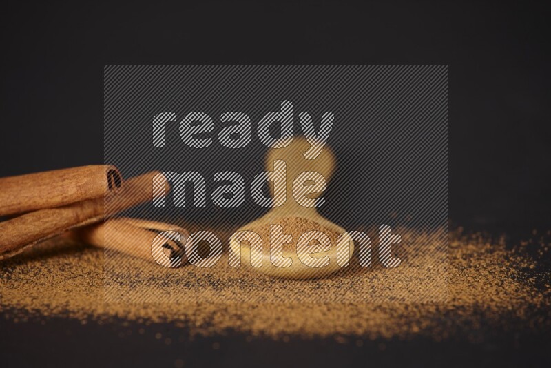 Cinnamon powder in a wooden spoon and cinnamon sticks beside it on black background