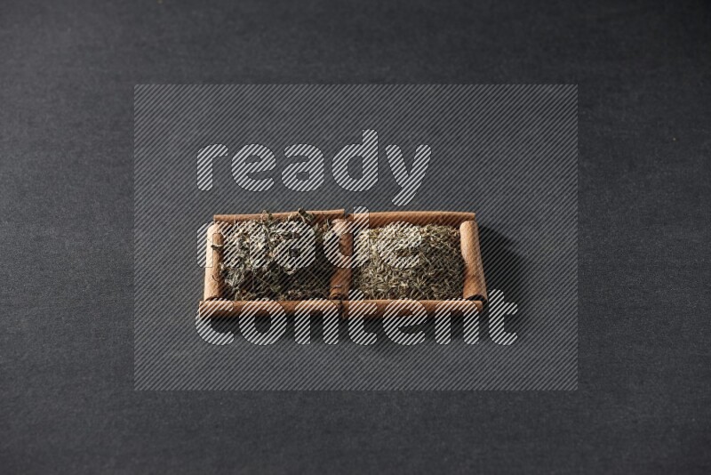 مربعان من أعواد القرفة ممتلئان بحبوب الكمون والريحان المجفف علي خلفية سوداء