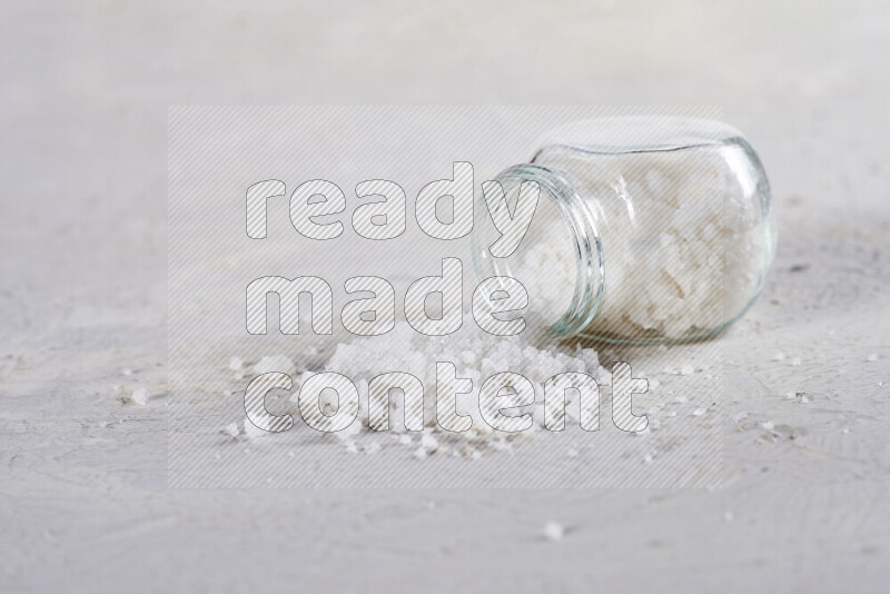 A glass jar full of coarse sea salt crystals on white background