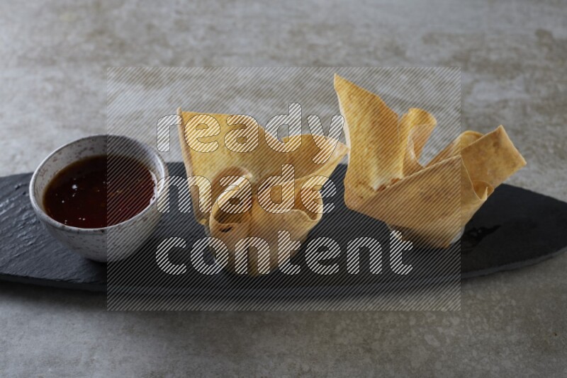 wonton cups with soy sauce ramkin on oval slate on grey textured counter top