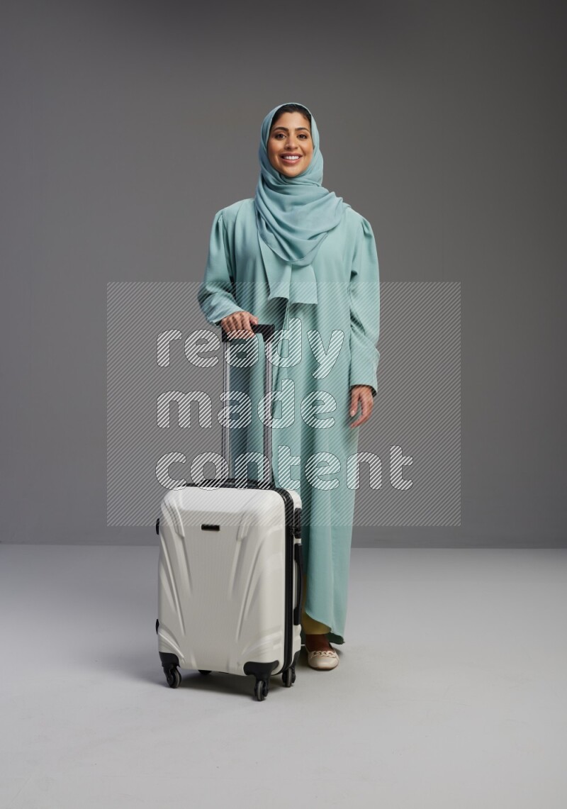 Saudi Woman wearing Abaya standing holding Travel bag on Gray background