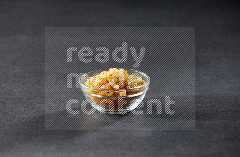 A glass bowl full of raisins on a black background in different angles