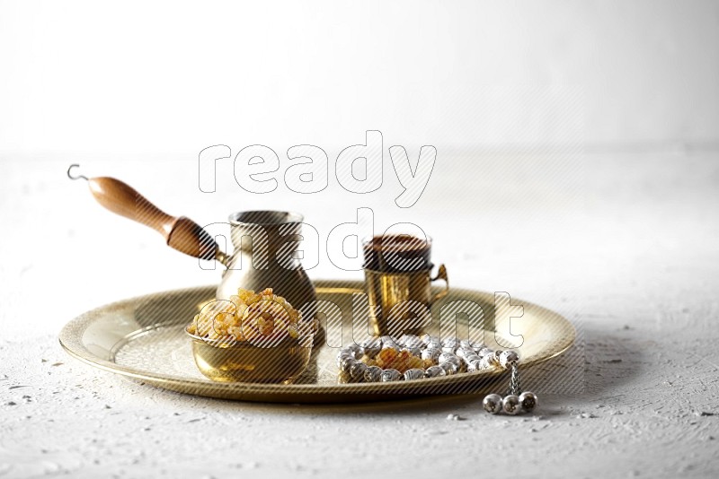 زبيب في وعاء معدني مع قهوة وسبحة على صينية علي خلفية بيضاء