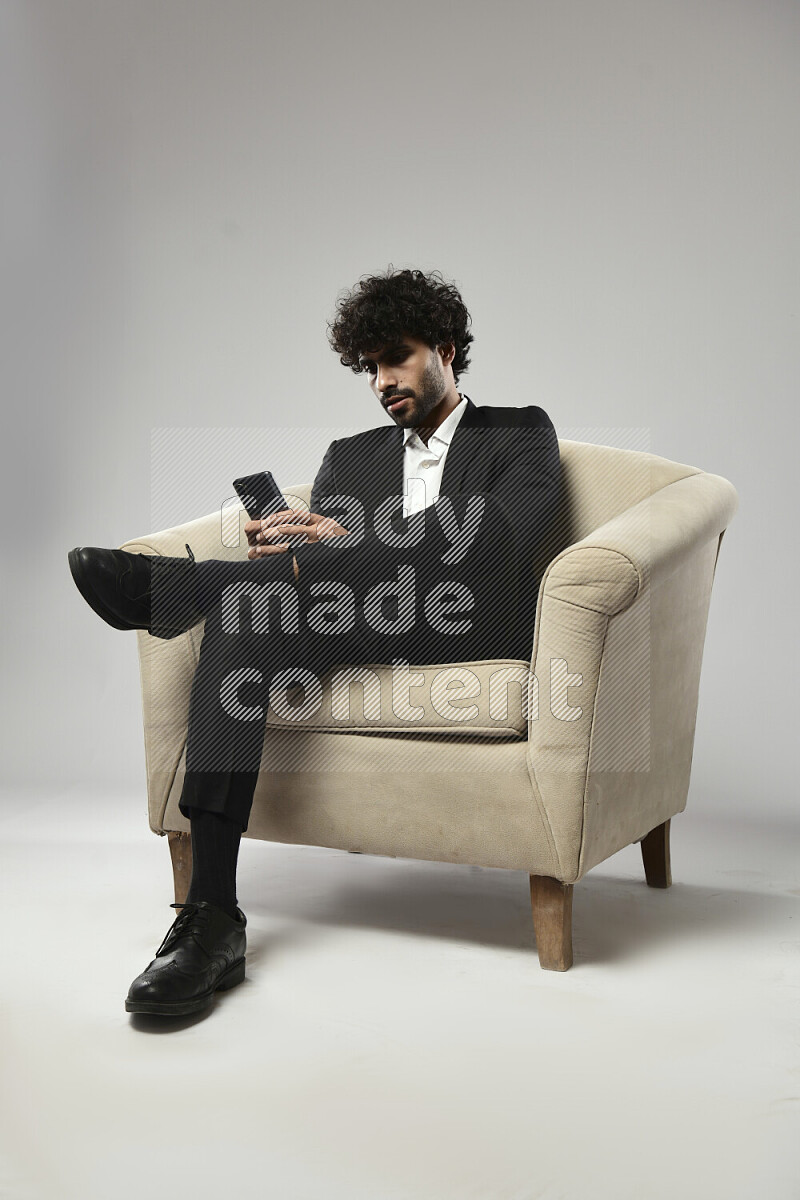 رجل يرتدي ملابس رسمية يجلس علي كرسي و يرسل رسائل نصية علي الهاتف علي خلفية بيضاء