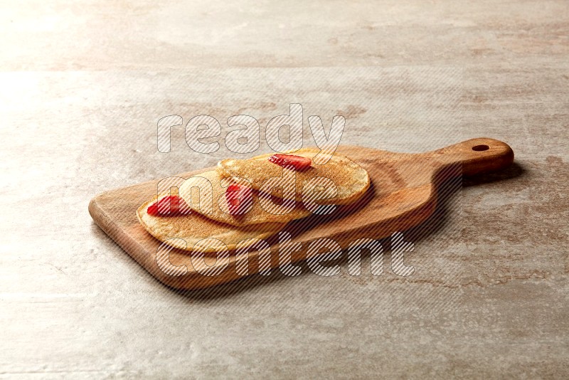 Three stacked strawberry pancakes on a wooden board on beige background