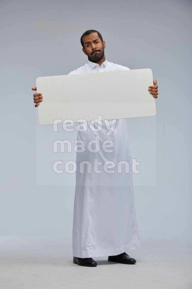 Saudi man wearing Thob standing holding board on Gray background
