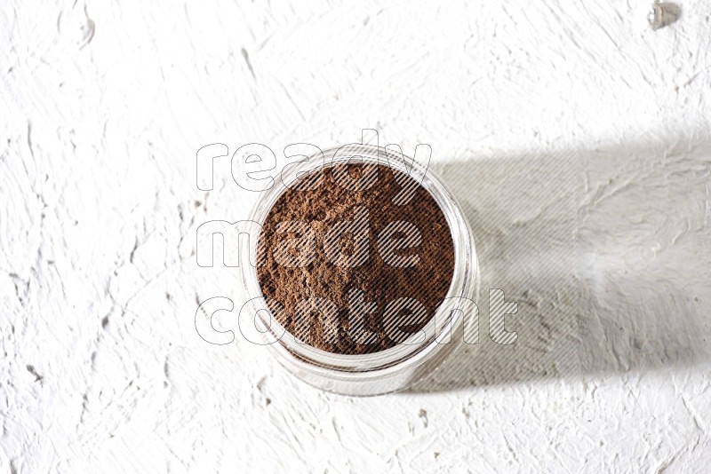 A glass jar full of cloves powder on a textured white flooring