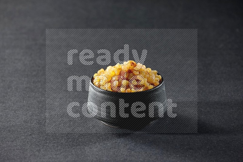 A black ceramic bowl full of raisins on a black background in different angles
