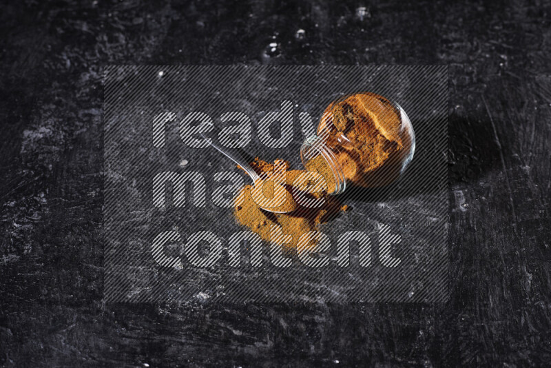 A glass jar full of ground paprika powder flipped with some spilling powder on black background