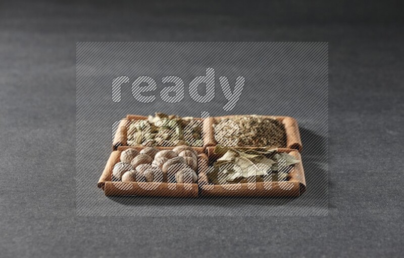 4 مربعات من عيدان القرفة ممتلئة بالكمون وحبوب الهيل وأوراق الغار وجوزة الطيب على أرضية سوداء