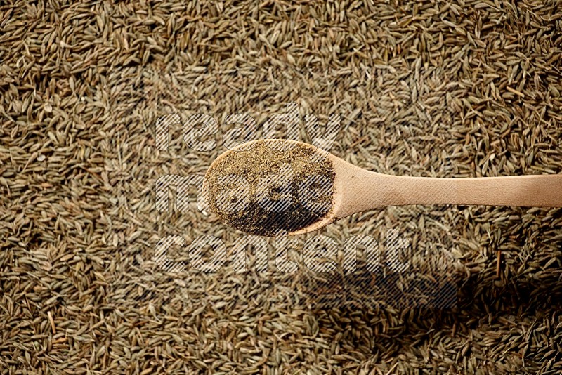 A wooden spoon full of cumin powder on a cumin seeds background