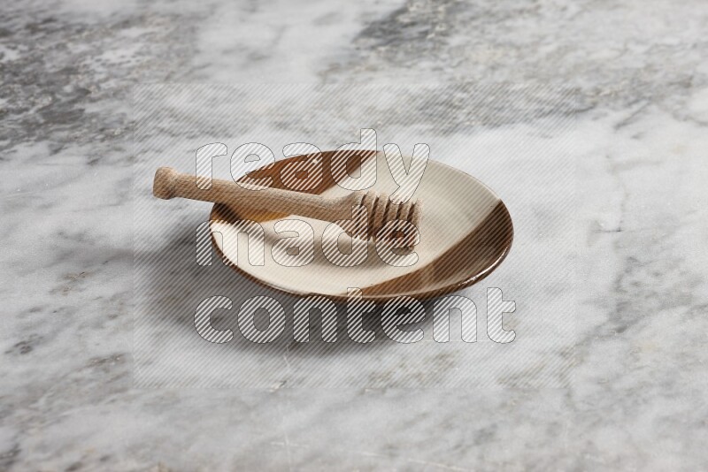 Multicolored pottery plate with wooden honey dipper in it on grey marble background