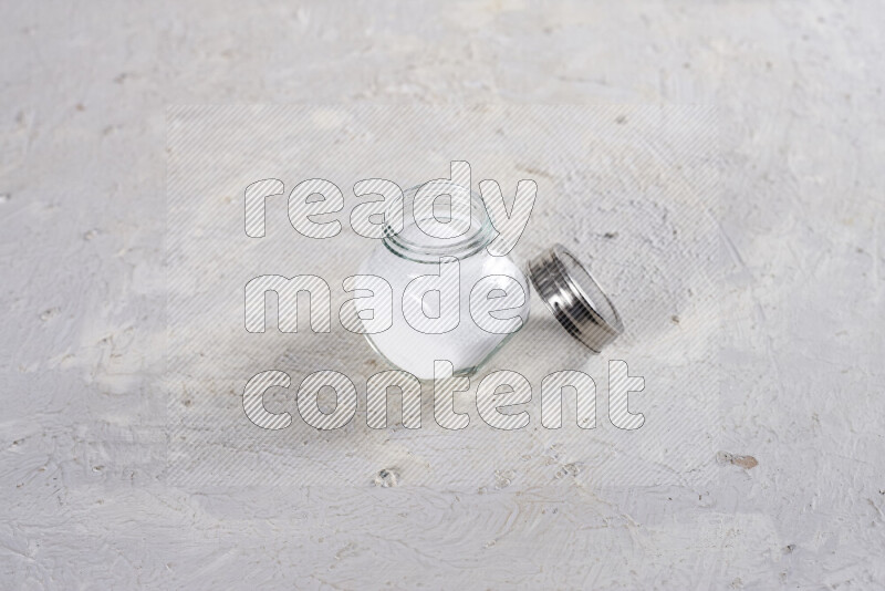 A glass jar full of fine table salt on white background