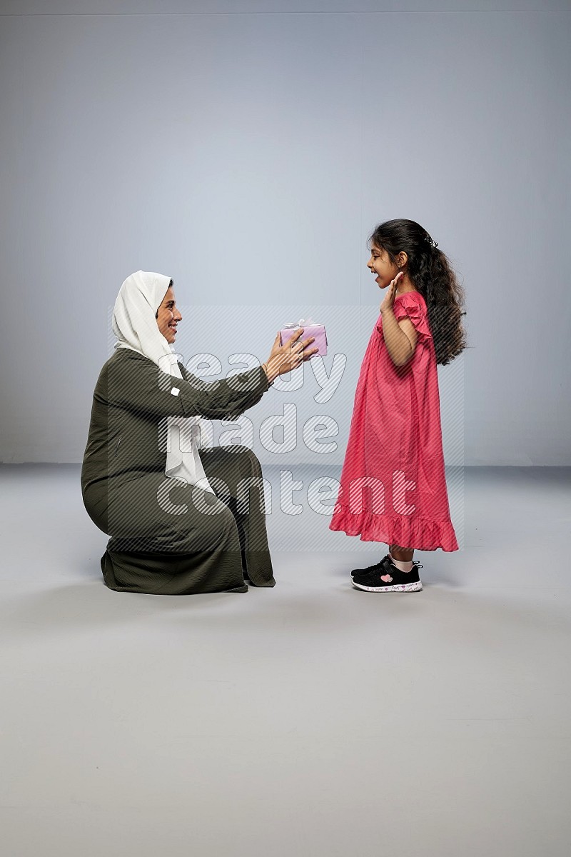 A girl giving a gift to her mother on gray background