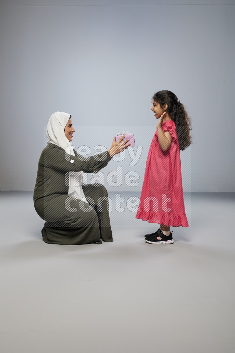 A girl giving a gift to her mother on gray background