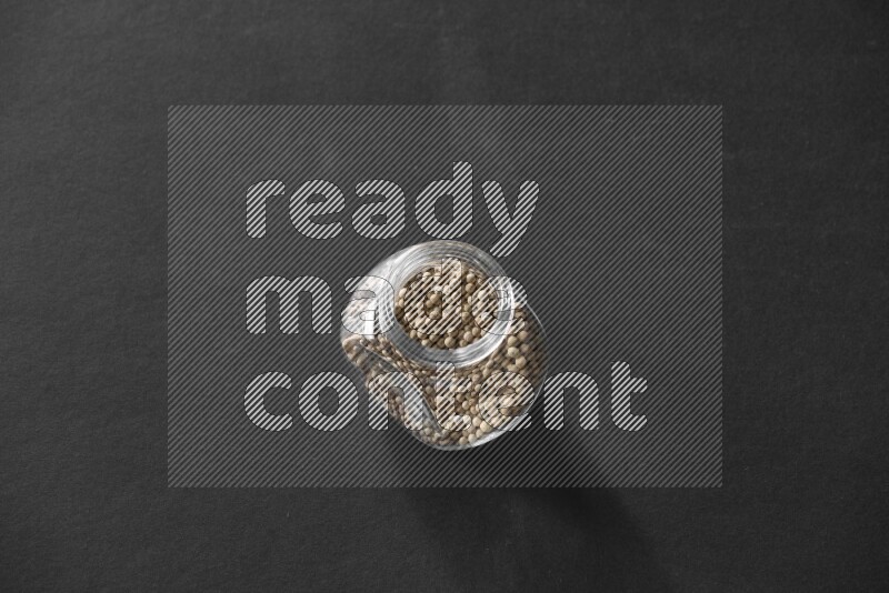 A glass spice jar full of white peppers on black flooring