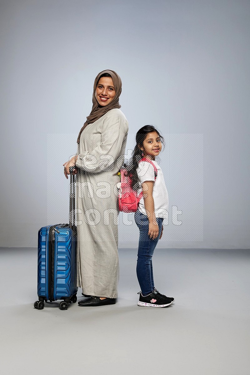 Mom and daughter standing pulling a carry-on bag on gray background
