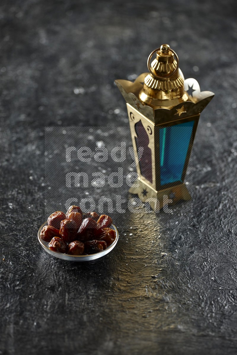 A golden lantern with different drinks, dates, nuts, prayer beads and quran on textured black background