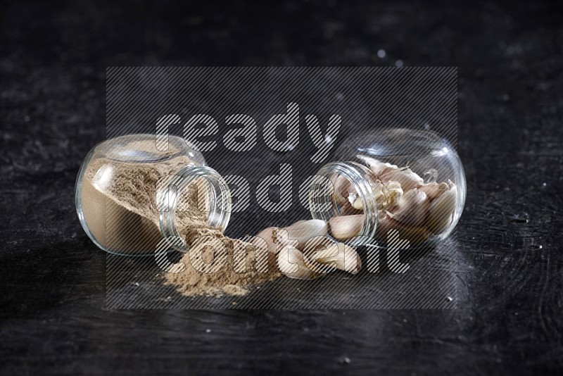 2 glass spice jars full of garlic cloves and powder flipped and the garlic came out on a textured black flooring in different angles