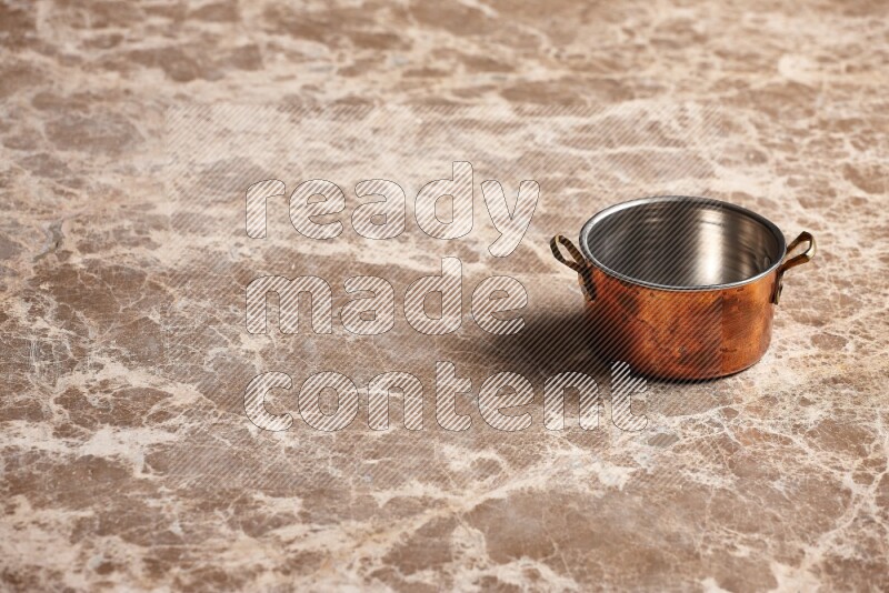 A small copper pot on beige marble background