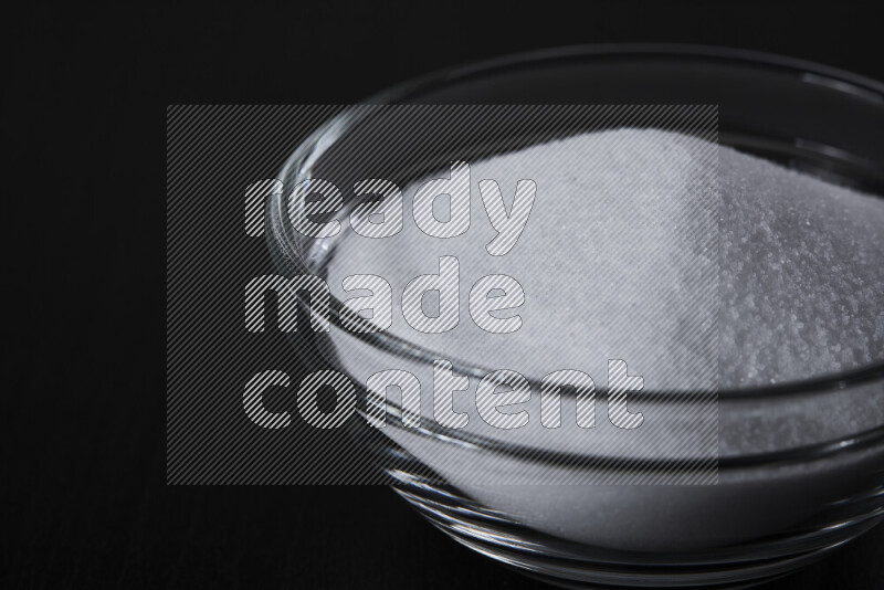 A glass bowl full of fine table salt on black background