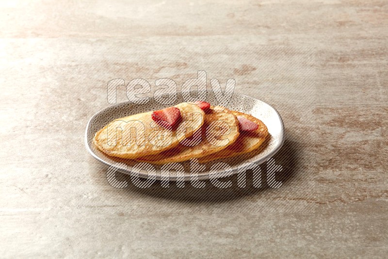 Three stacked strawberry pancakes in an irregular plate on beige background
