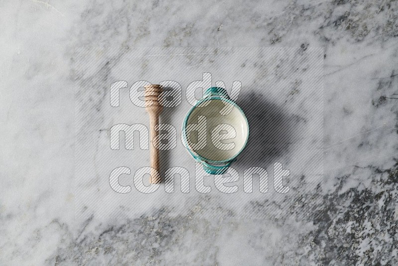 Multicolored Pottery Bowl with wooden honey handle on the side on grey marble flooring, Top view