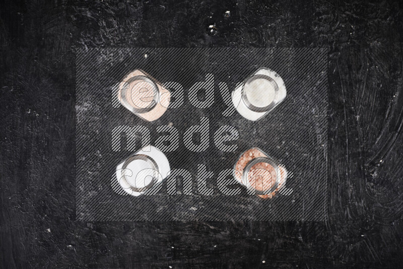 4 glass jars filled with table salt, coarse sea salt, fine himalayan salt and coarse himalayan salt on black background