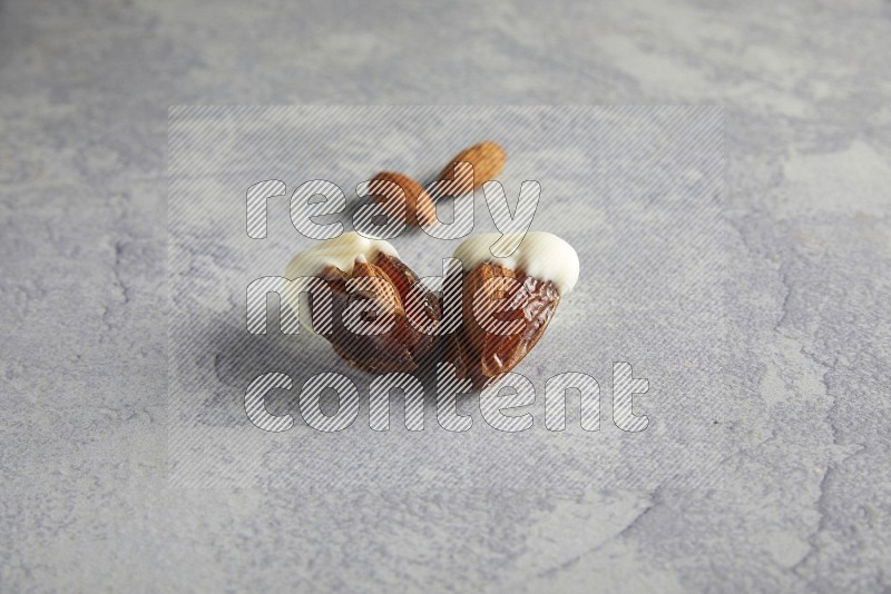 two almonds stuffed dates covered with white chololate with unroasted almonds on a light grey background