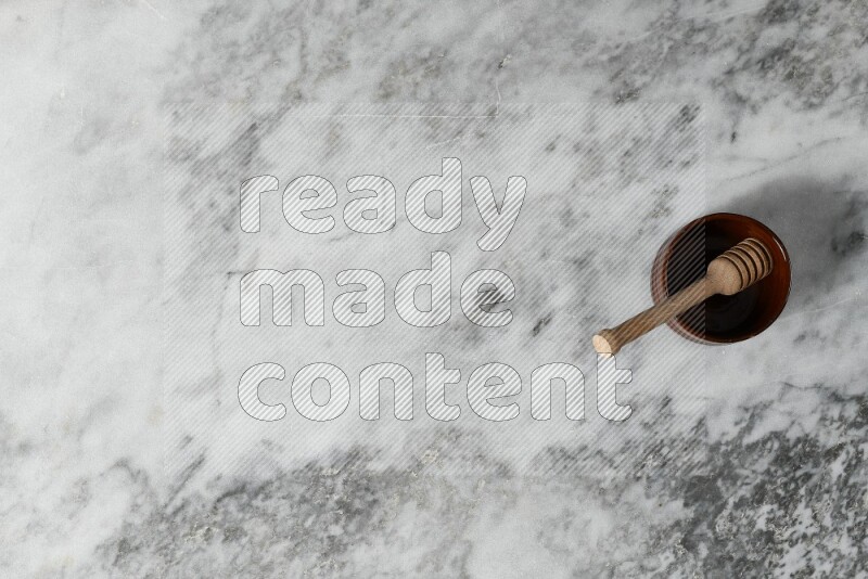 Brown pottery bowl with wooden honey dipper in it on grey marble background
