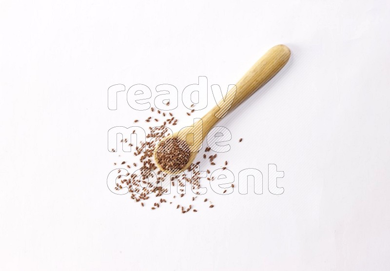 A wooden spoon full of flax seeds on a white flooring