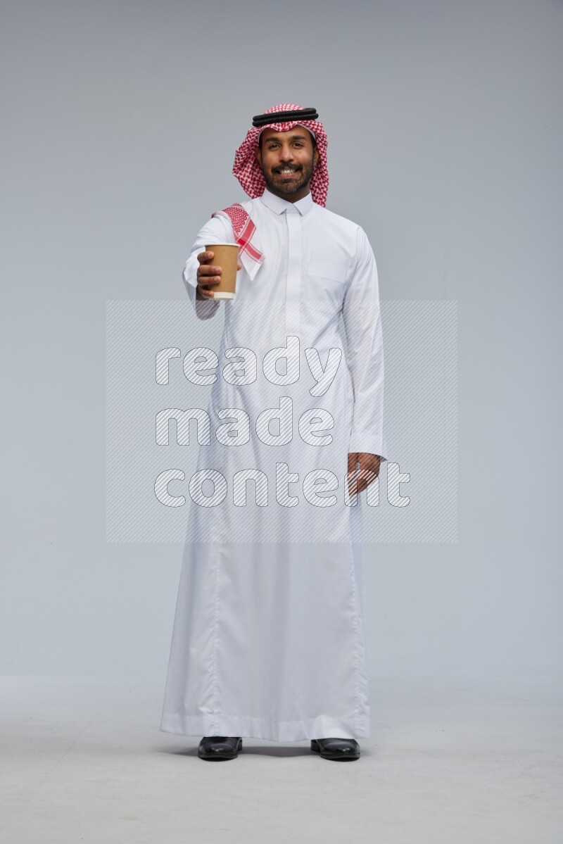 Saudi man Wearing Thob and shomag standing holding paper cup on Gray background