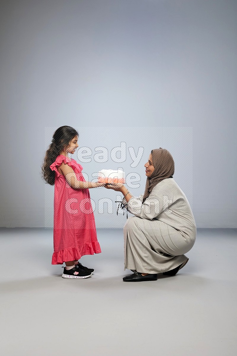 A mother giving a cake to her daughter on gray background