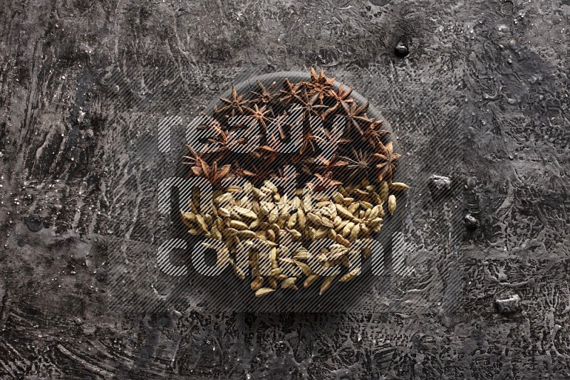 Cardamom and star anise on a black plate on textured black background