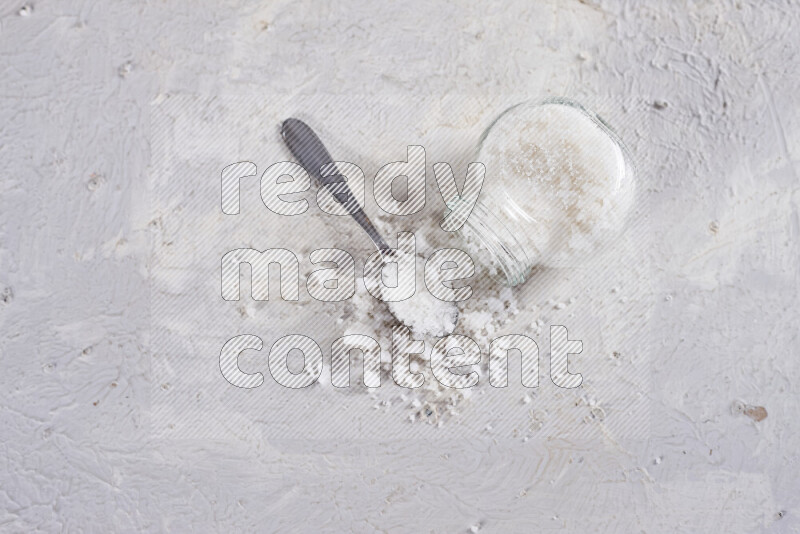 A glass jar full of coarse sea salt crystals on white background