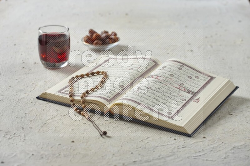 Quran with dates, prayer beads and different drinks all placed on textured white background